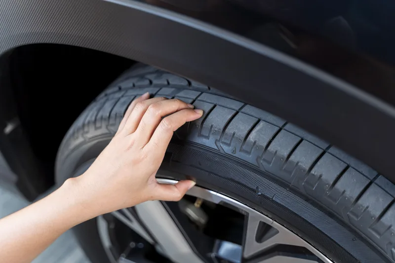 Hand running along a car tire's tread, checking for a nail