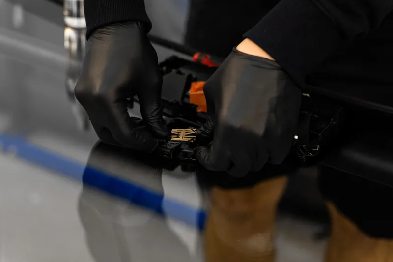 Gloved hands fitting a driver-assist camera module to its bracket behind a new windshield