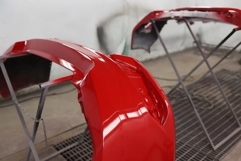 Two freshly painted red bumper covers on stands, curing in the paint shop