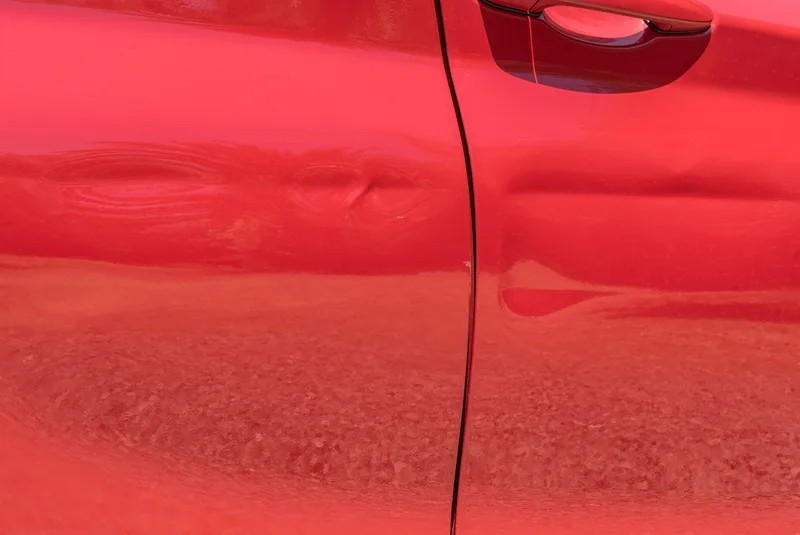 Close view of a long dent running across two red car doors