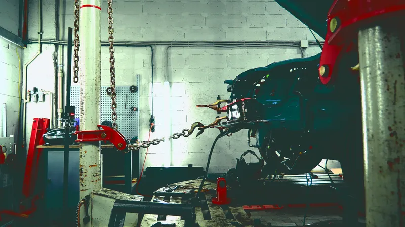 Damaged car body clamped to a frame straightening machine, with chains pulling the front structure back into place