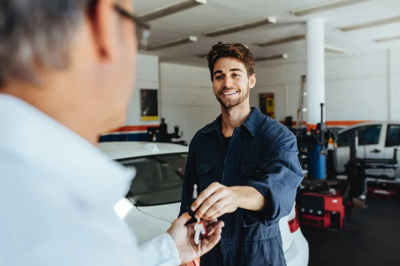 Smiling shop employee handing car keys back to a customer in the service area