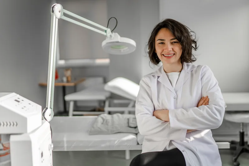 Dr. Amara Sethi in a white coat, seated beside the magnifying lamp in a Lumen treatment room