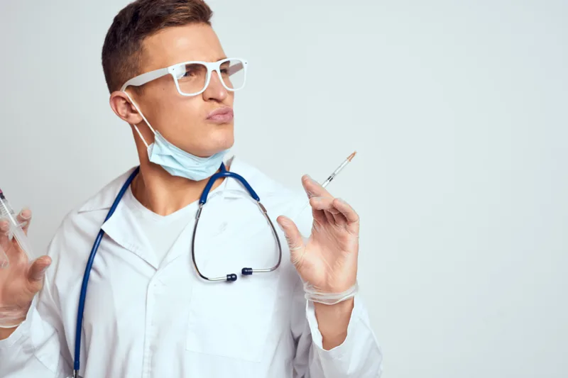 Jonas Feld, nurse practitioner, in a white clinical coat with a stethoscope, holding a syringe