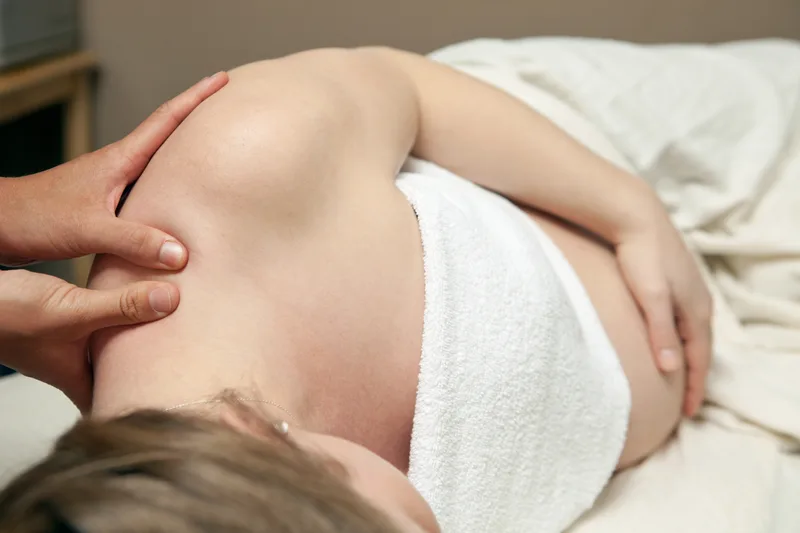 Pregnant client resting on her side while a therapist works carefully through her shoulder and neck