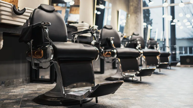 Row of black leather barber chairs under bright windows in an open barbershop