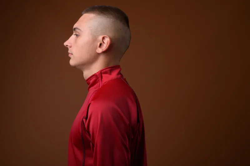 Side profile of a young man with a short crew cut wearing a red jacket