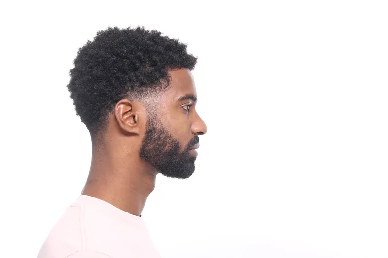 Side profile of a man with natural curls on top, a low taper and a lined beard