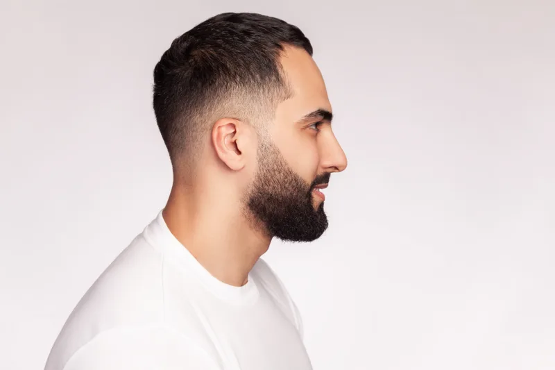 Side profile of a man with a mid fade, short textured top and a full shaped beard