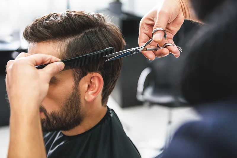 Barber cutting the top of a client's hair with scissors over a comb