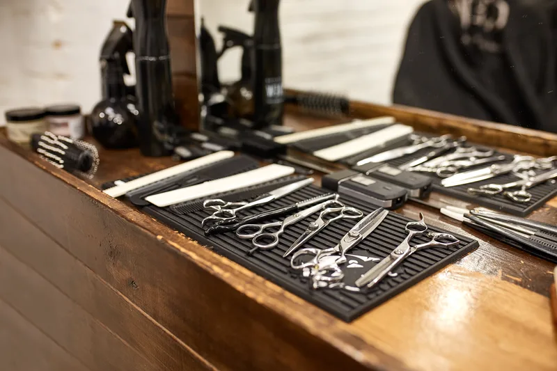 Scissors, combs and clippers laid out on a black mat on a wooden barber station
