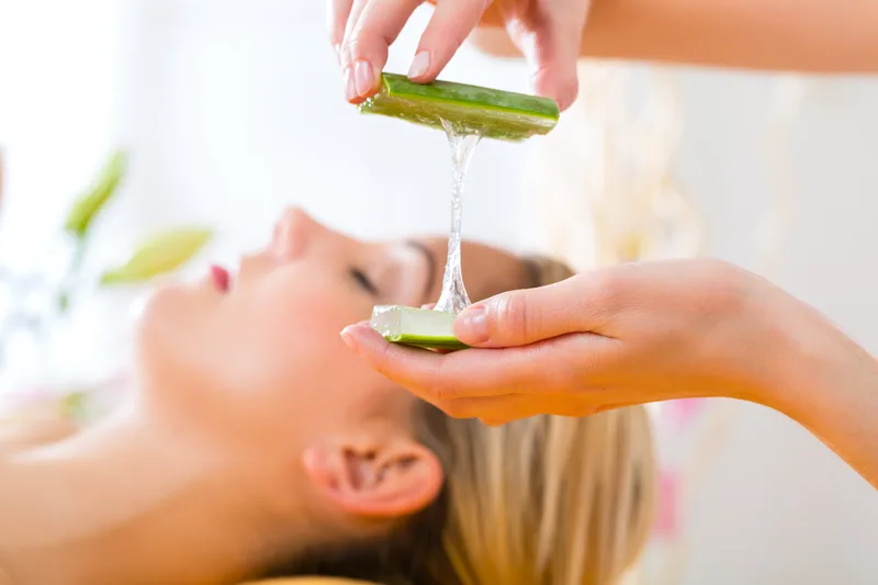 Clear aloe gel dripping from a fresh leaf onto a client's cheek during a calming facial