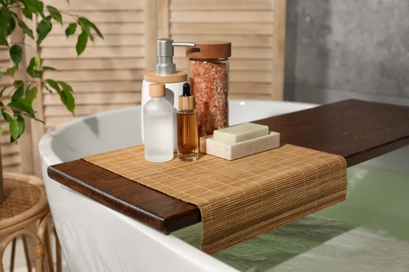 A few plain skincare bottles and a bar of soap on a wooden bath tray