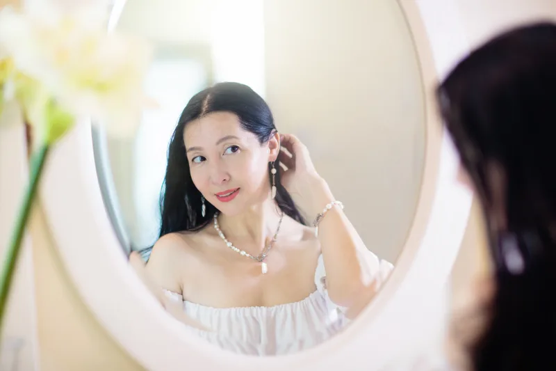 A woman checking her skin in a round vanity mirror in soft morning light