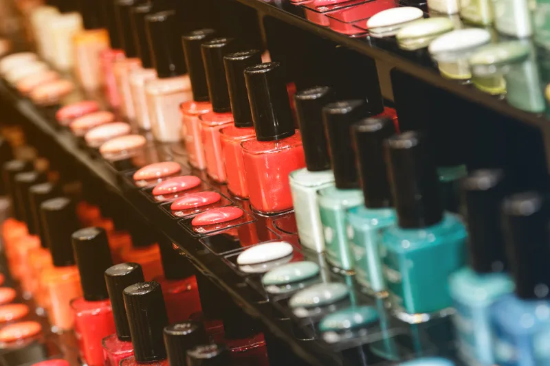 Shelves of nail polish bottles arranged in a colour gradient from corals and pinks to teals
