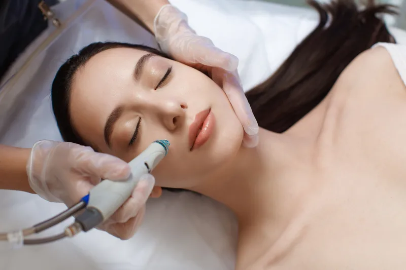 Close-up of a hydradermabrasion wand gliding across a relaxed guest's cheek