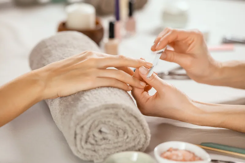 A manicurist working on a guest's nails over a rolled grey towel at a tidy station