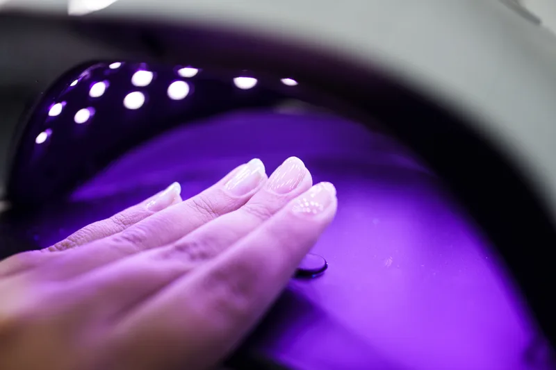 A hand resting inside a violet-lit LED curing lamp during a gel manicure