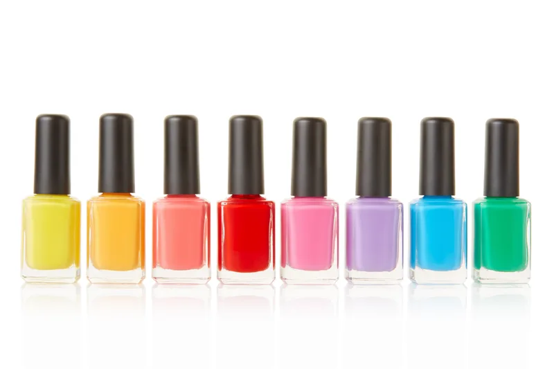 Eight nail polish bottles in a rainbow row from yellow through red, pink, lilac, blue, and green