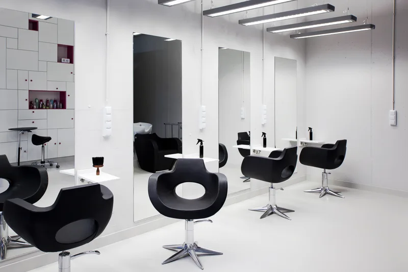Minimal styling floor with sculptural black chairs at tall frameless mirrors under linear studio lights