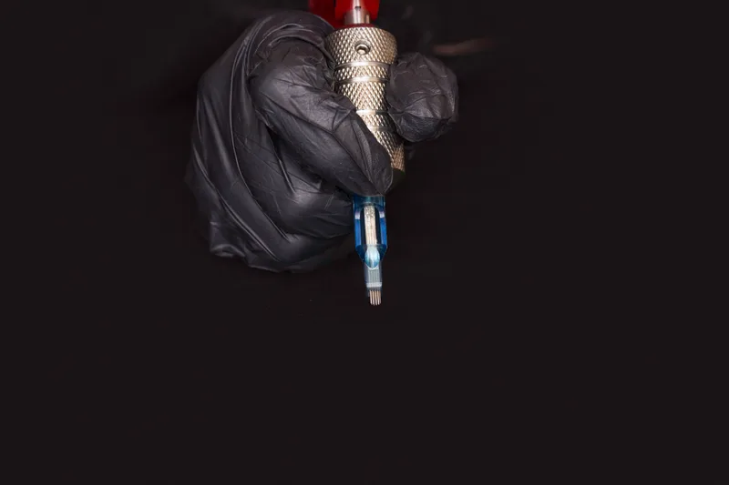 Gloved hand holding a tattoo machine fitted with a sealed, single-use needle cartridge