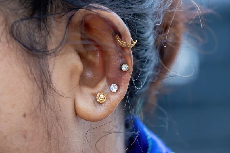 Close view of a healed ear with lobe, helix and cartilage piercings in small gold and stone studs