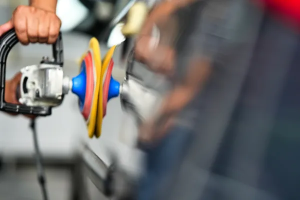 Auto detailer machine-polishing a car's paint to a high-gloss finish inside a detailing shop bay