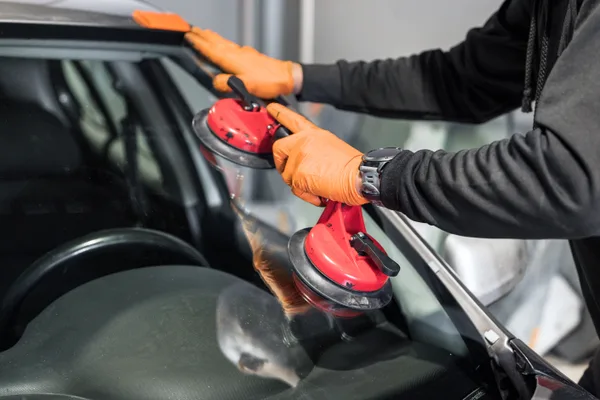 Auto glass technician fitting a new windshield to a vehicle in a service bay