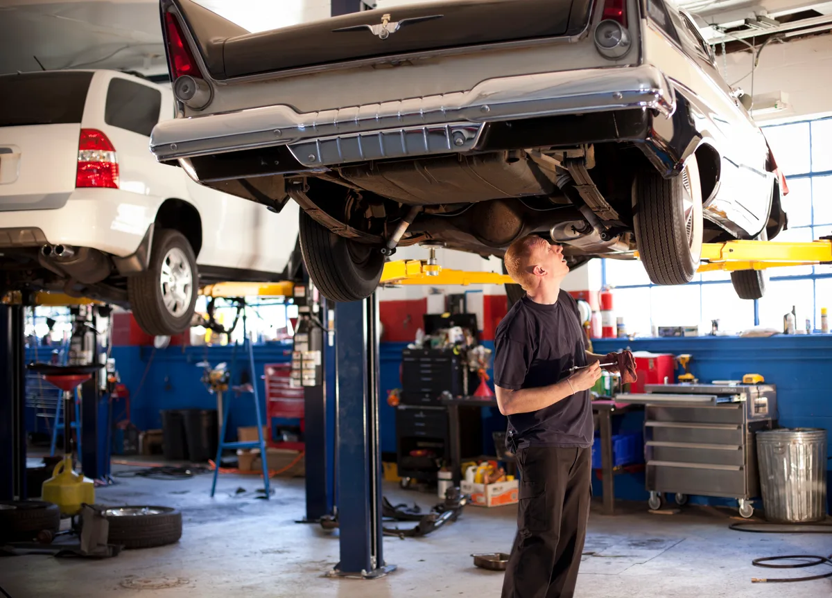 Mechanic inspecting a vehicle on a hydraulic lift in a busy auto repair service bay