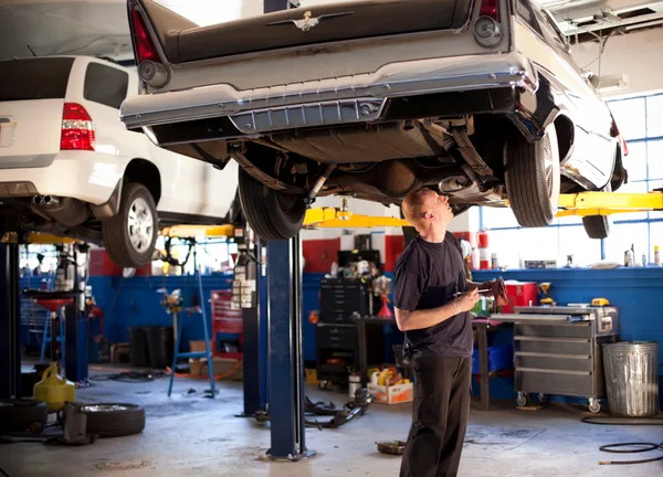 Mechanic inspecting a vehicle on a hydraulic lift in a busy auto repair service bay