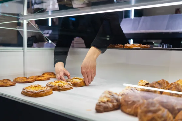 A baker arranging fresh croissants and pastries in a bakery display case