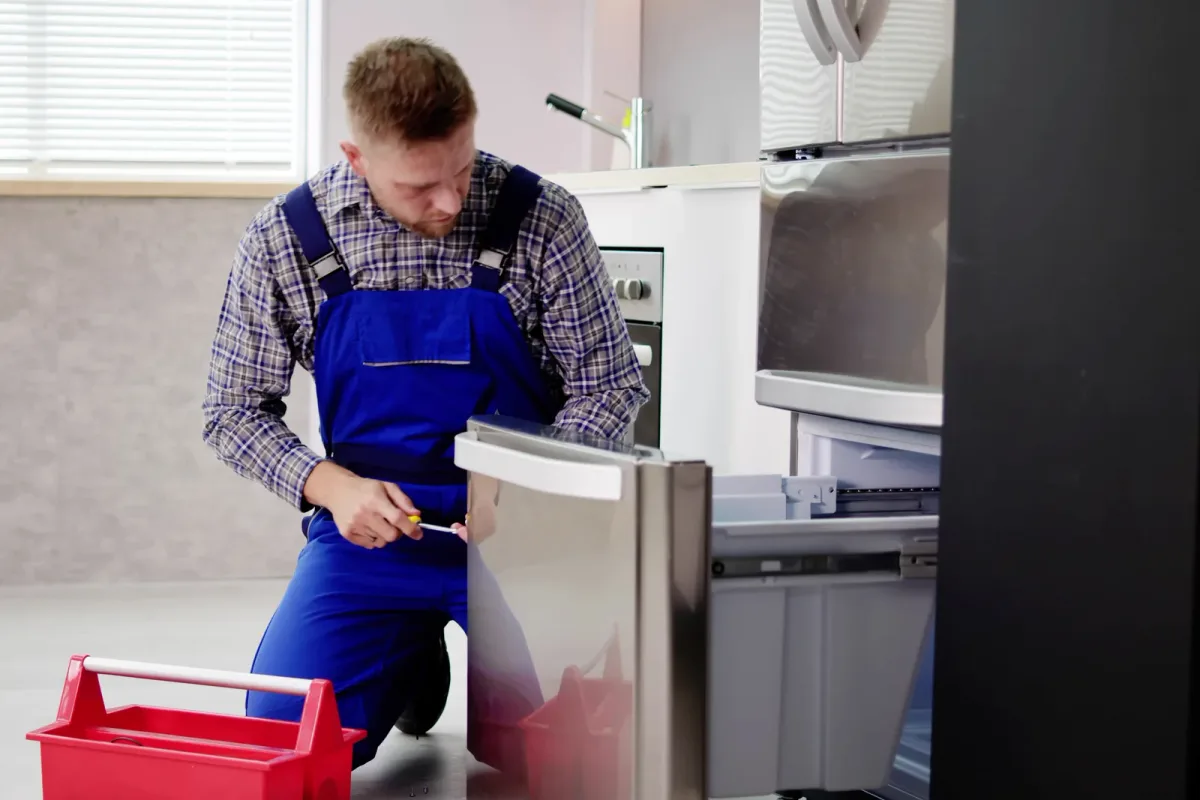 An appliance repair technician kneeling beside an open dishwasher in a customer's kitchen