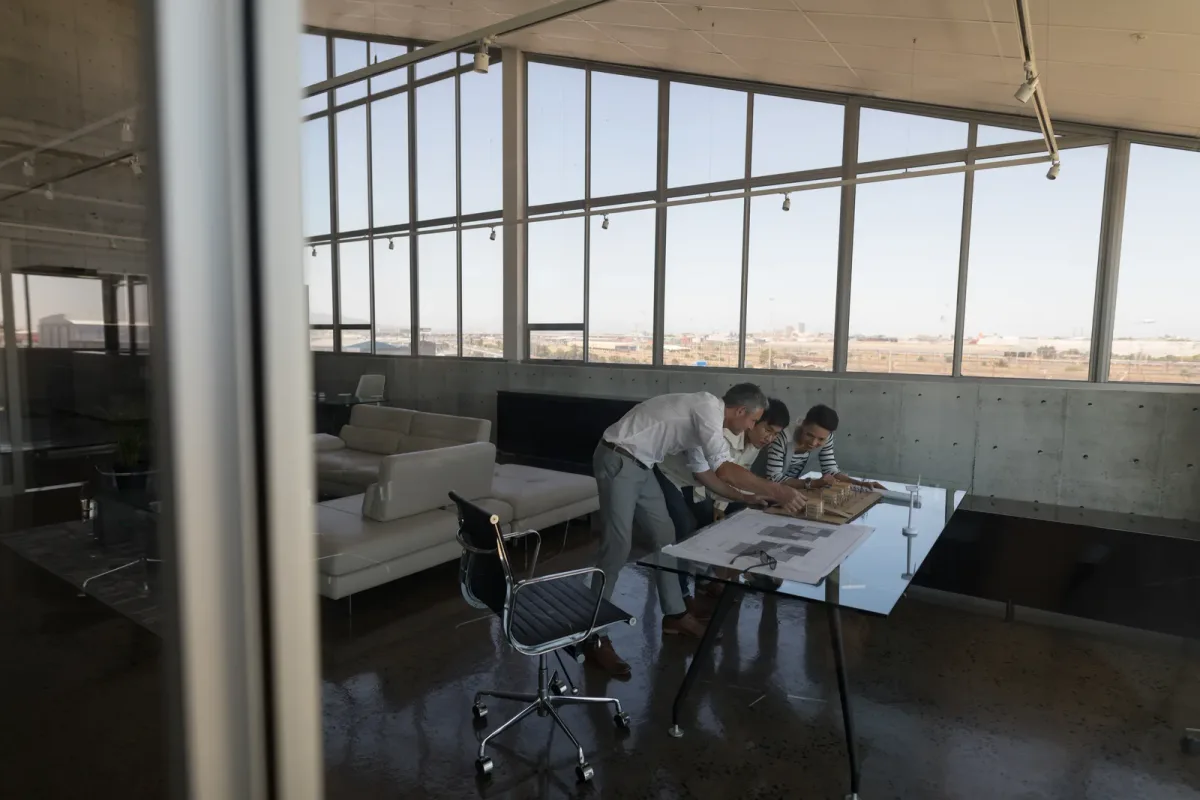 Architect reviewing blueprints and a scale model of a custom home with a client at a drafting table