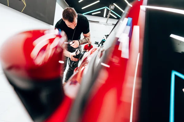 Detailer machine-polishing a car's paint to a high-gloss finish inside a detailing shop bay