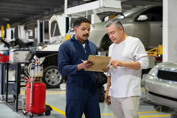 Auto repair shop owner reviewing a service estimate with a customer in the garage
