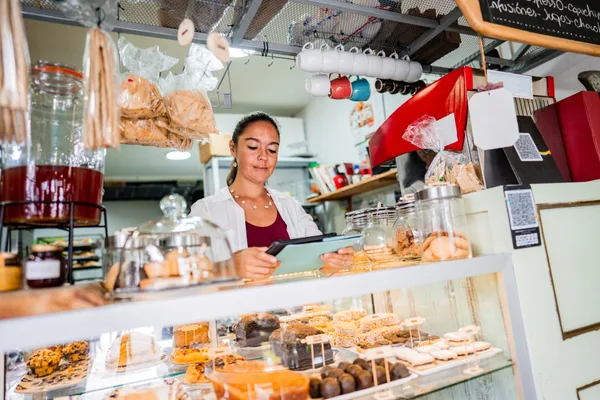 Bakery owner reviewing performance on a tablet behind a display case of fresh pastries and cakes