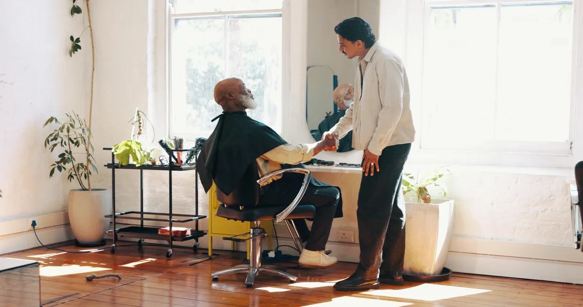 A barbershop owner shaking hands with a marketing consultant across the front desk of the shop