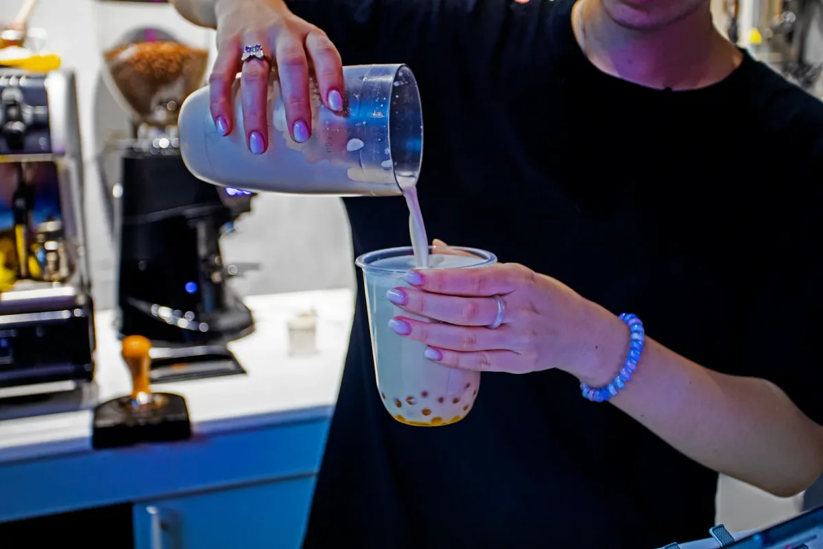 A barista preparing a customized bubble tea order with tapioca pearls behind a busy shop counter