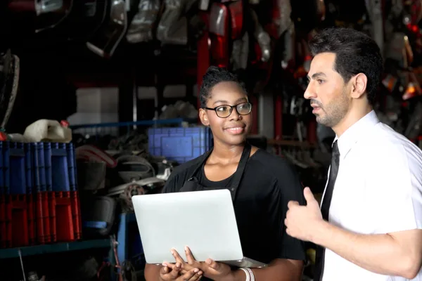 Collision repair shop owner reviewing marketing performance on a laptop with an advisor in an auto body office