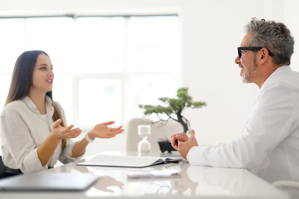 A board-certified plastic surgeon reviewing options with a patient during a consultation in a bright, modern clinic
