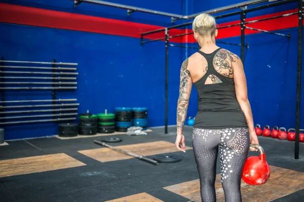 A CrossFit gym owner reviewing membership numbers on a tablet beside a rack of barbells