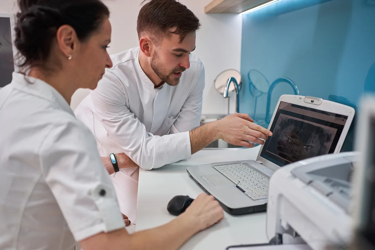 A dental practice owner reviewing new-patient marketing results on a laptop with a team member in a bright modern clinic