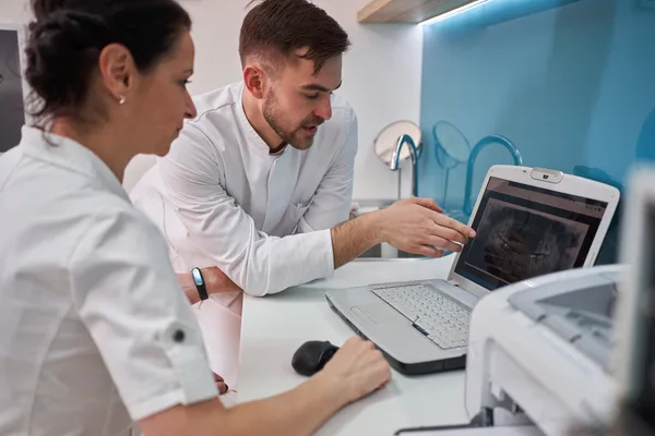 A dental practice owner reviewing new-patient marketing results on a laptop with a team member in a bright modern clinic