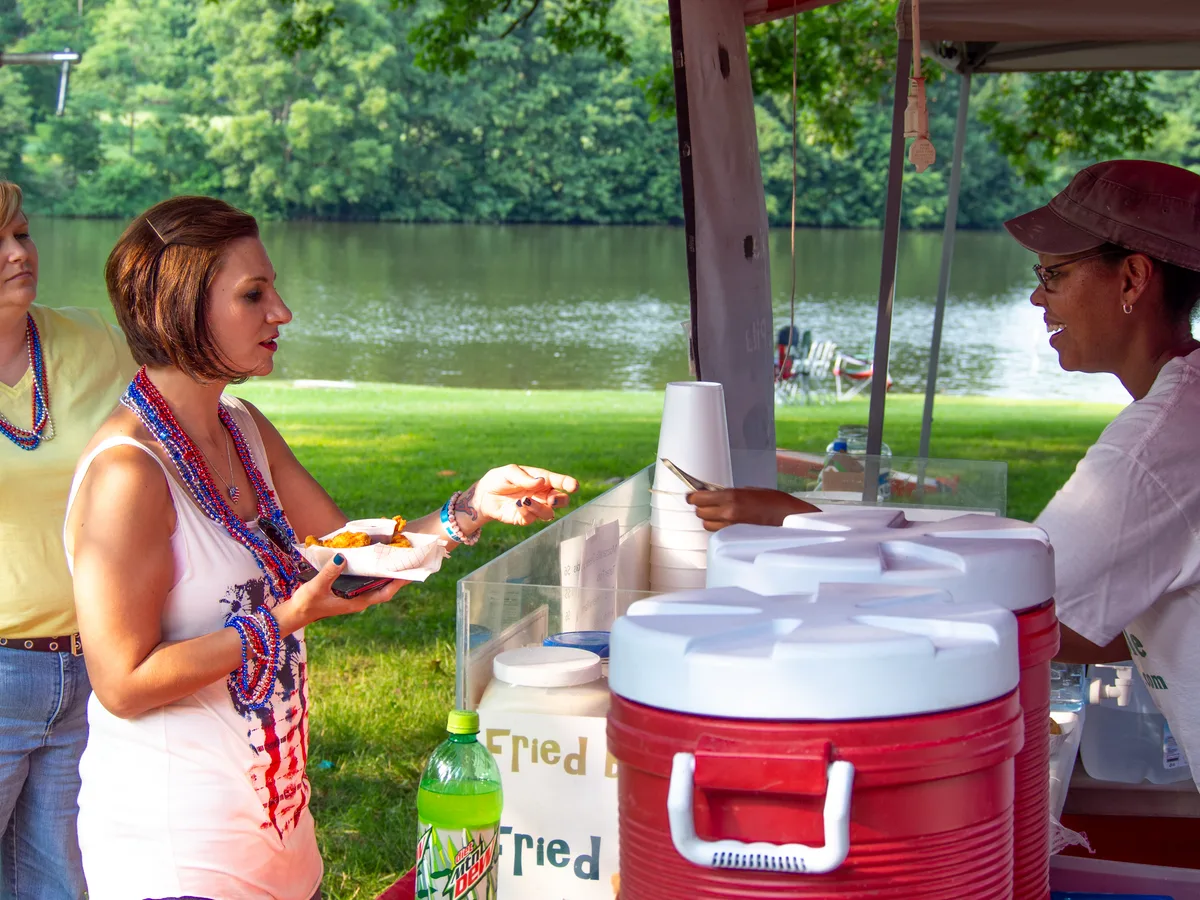 A food truck owner handing an order to a customer at a busy outdoor event