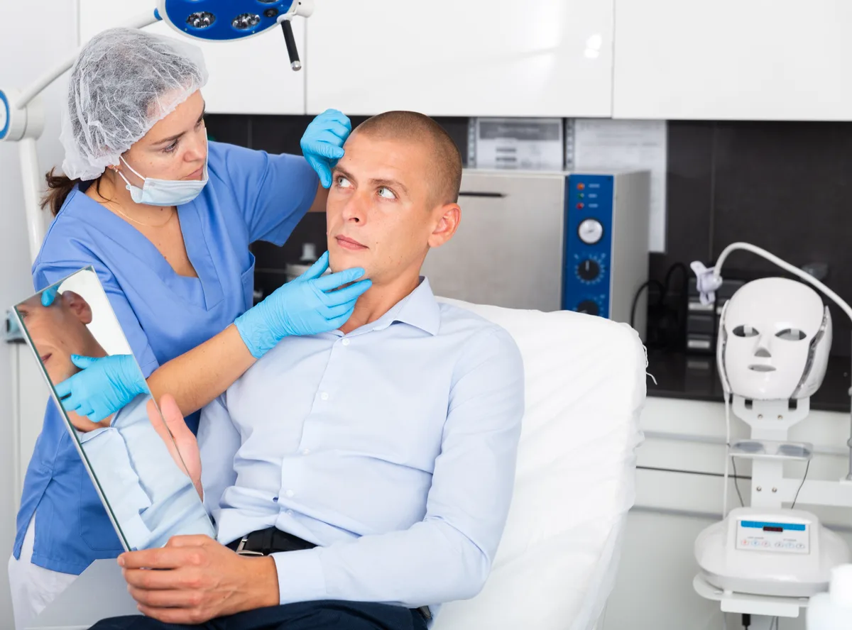 A hair restoration surgeon reviewing a treatment plan with a male patient in a bright modern clinic consultation room