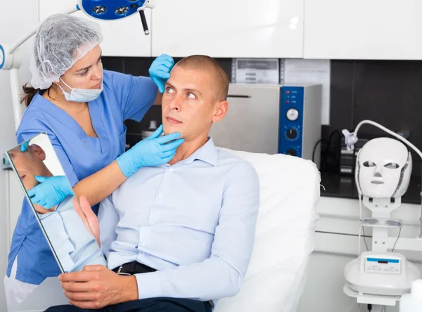 A hair restoration surgeon reviewing a treatment plan with a male patient in a bright modern clinic consultation room