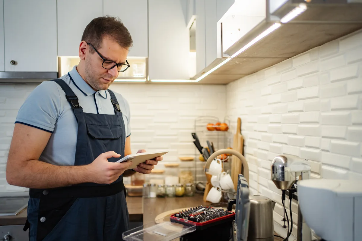 A handyman checking his job schedule on a tablet inside a homeowner's kitchen