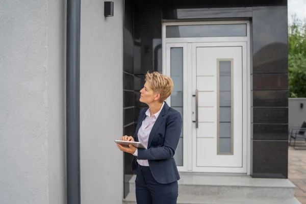 Home inspector examining the exterior of a house with a tablet during a property inspection