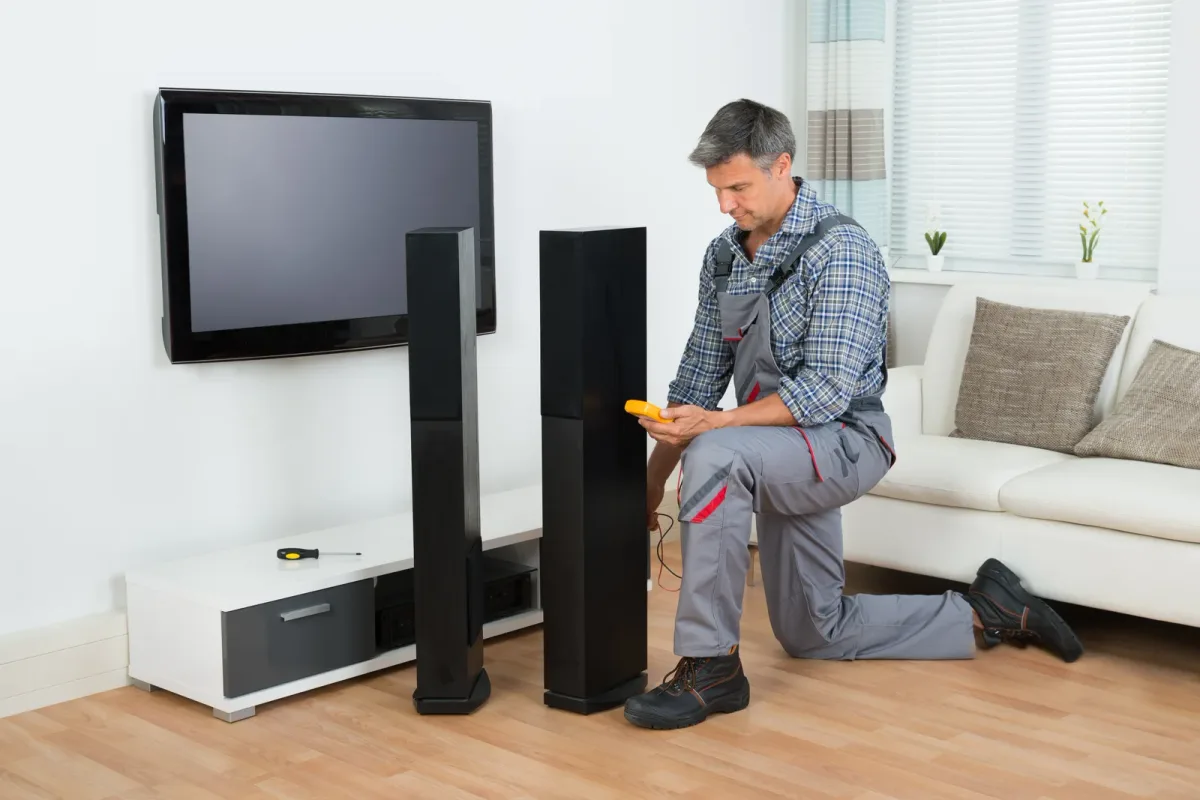 An installer mounting a large flat screen TV in a custom home theater with tiered leather seating