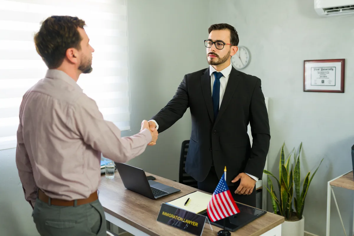 An immigration attorney shaking hands with a client across a desk in a law office